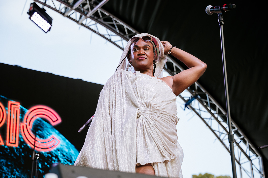 A performer in a silver outfit captivates the audience on stage, with colorful lighting and a microphone in the background.
